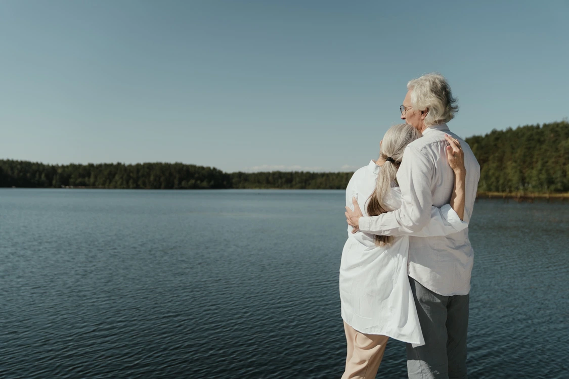 older couple hugging, looking over a lake